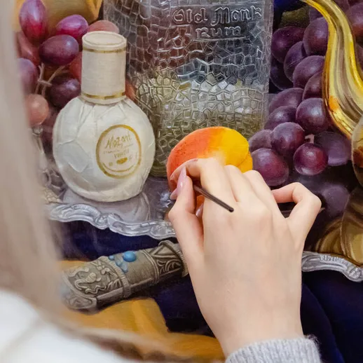 Художник работает над натюрмортом с фруктами и предметами быта