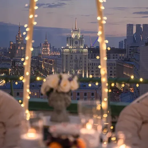 Уютный столик на крыше с видом на вечернюю Москву и огни города в момент заката