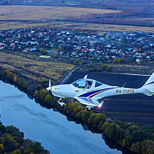 Летящий легкомоторный самолет над рекой и сельской местностью во время заката