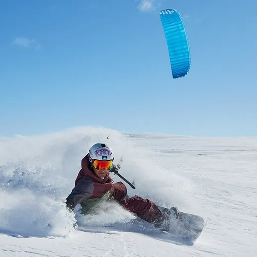 Кайтбордист, скользящий по снежному склону под ярким голубым небом в зимний день