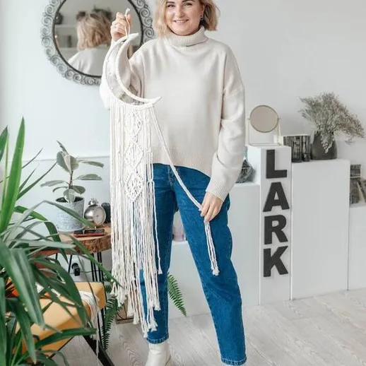 Женщина в свитере показывает произведение искусства в интерьере с растениями и часами