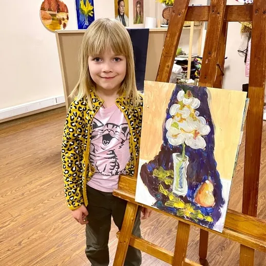 Девочка позирует рядом с живописью на выставке в художественной школе