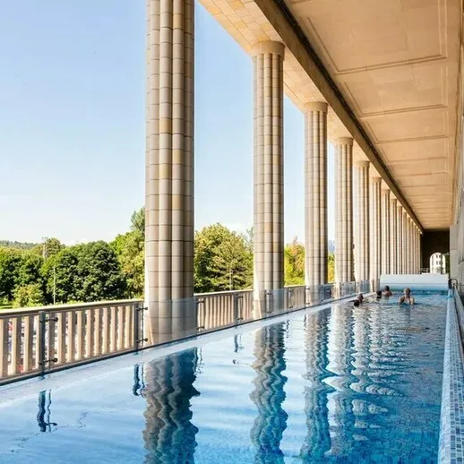 Современный бассейн с колоннами и прозрачной водой на фоне зелени в солнечный день