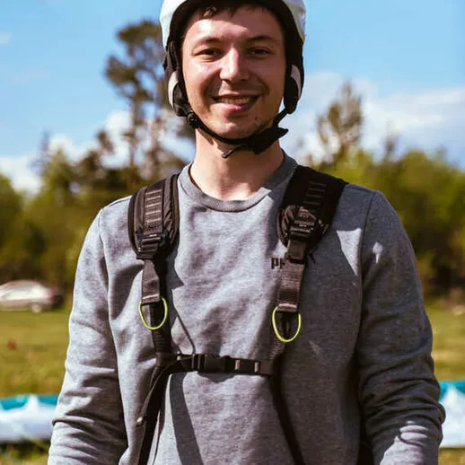 Молодой человек в шлеме готовится к парапланеризму на зеленом поле в солнечный день