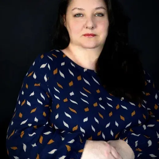 Женщина в синем платье с узором на темном фоне уверенно позирует для портрета в студии