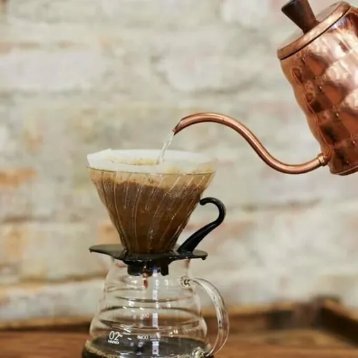 Приготовление кофе с помощью металлической воронки и чайника на деревянном столе в уютной обстановке