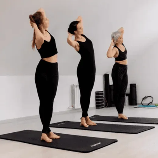 Тренировка группой женщин в черной спортивной одежде на ковриках в зале для фитнеса