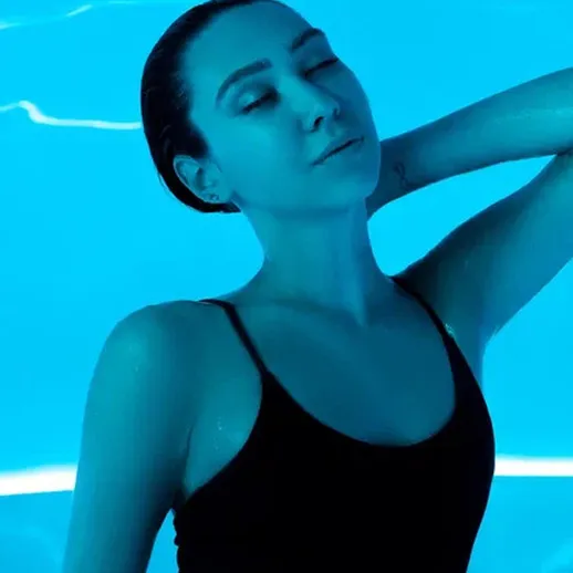 Женщина в черном купальнике позирует под ярким водным светом