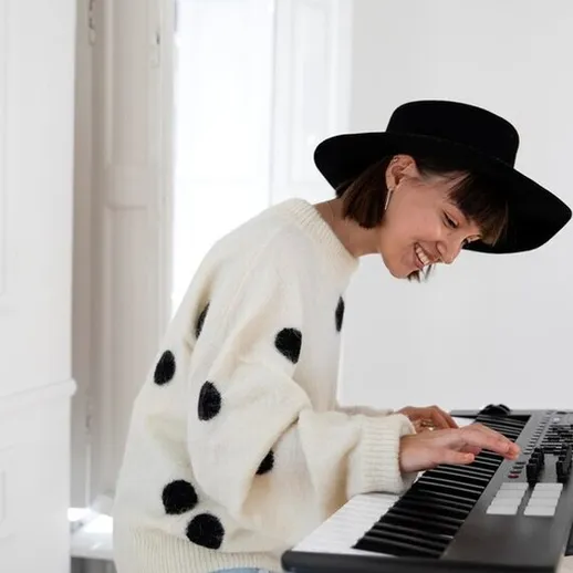 Музыкантка играет на клавиатуре в светлой комнате с крупными черными горохами на свитере