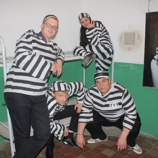 Группа людей в полосатой одежде позирует в тюремной камере с графикой на стене