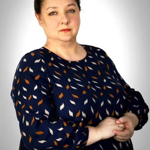 Женщина в синем платье с узором на фоне светлых тонов, позирующая с уверенностью и спокойствием