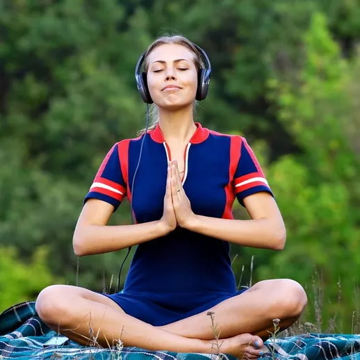 Молодая женщина медитирует на траве в парке, слушая музыку в наушниках, наслаждаясь природой и спокойствием