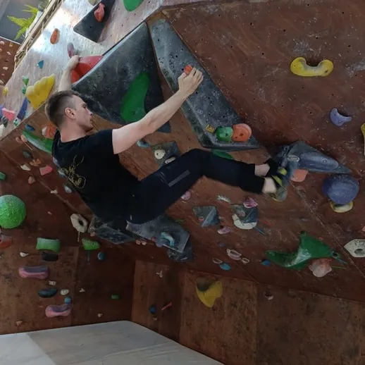 Соревновательный скалолаз на искусственном маршруте в спортзале, работающий над сложным восхождением