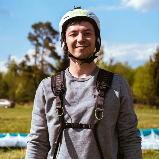 Парапланерист в шлеме на ярком фоне природы, готовый к полёту в солнечный день