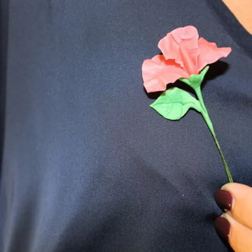 Женщина держит бумажную розу на синем топе в солнечном свете на фоне улицы