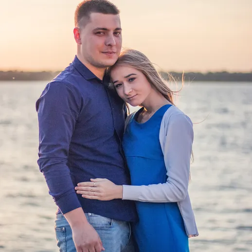 Молодая пара на фоне заката у реки, наслаждающаяся моментом близости и романтики