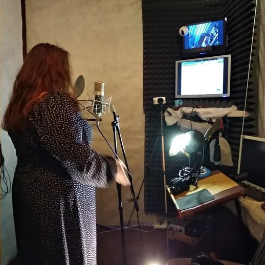 Запись голоса в студии на заказ, женщина стоит с микрофоном в уютной звукозаписывающей комнате