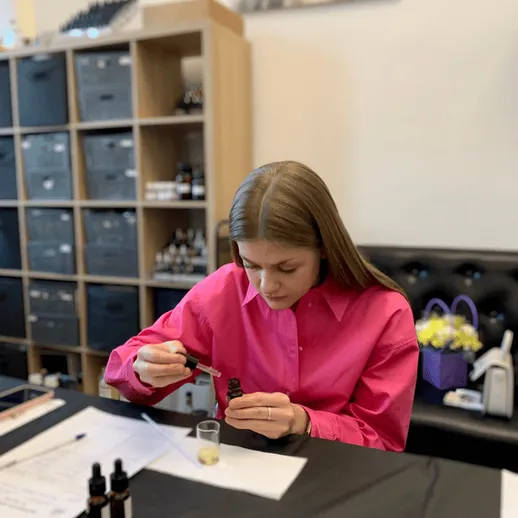 Женщина в розовой рубашке экспериментирует с маслами в лаборатории во время создания косметического продукта