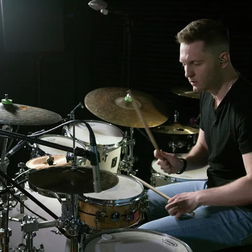 Молодой музыкант играет на ударных в студии звукозаписи во время вечерней сессии