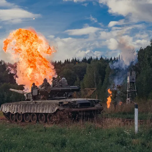 Танк на учении выделяет огненные заряды в лесистой местности под ясным небом