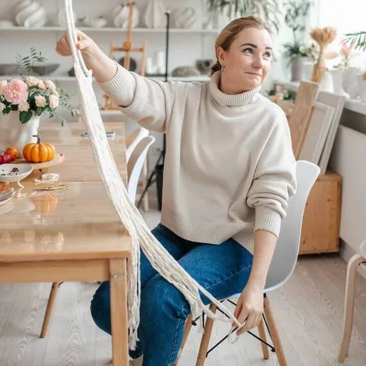 Женщина занимается рукоделием в уютной мастерской с натуральными материалами и осенним декором на столе