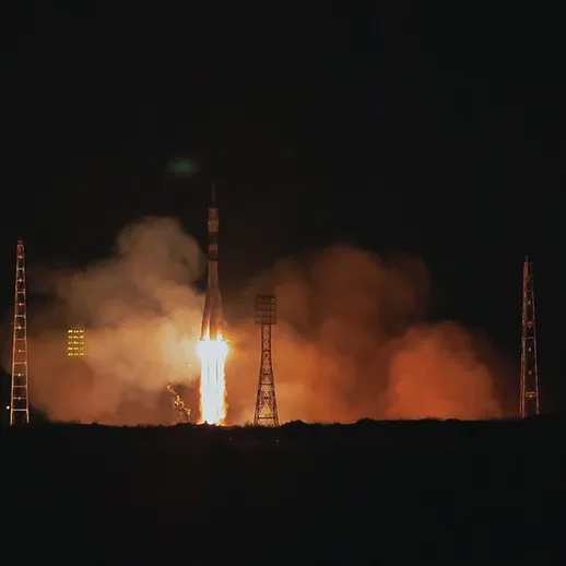 Запуск ракеты в ночном небе над космодромом, освещающим окрестности ярким пламенем