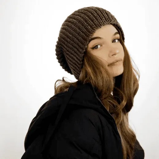 Молодая девушка с длинными волосами в шапке на светлом фоне, позирует в теплой одежде осенью