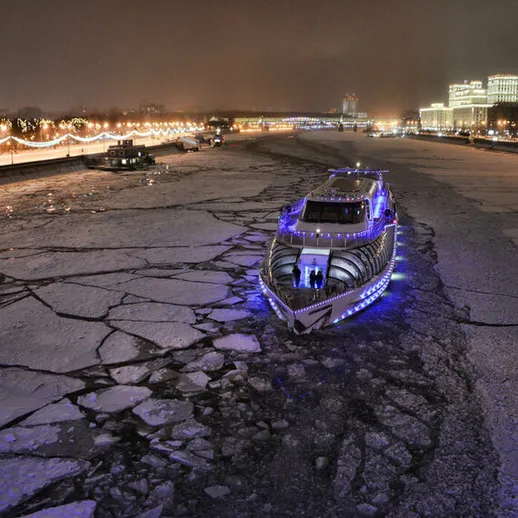 Красивый прогулочный корабль на реке в ночное время, окруженный ледяными плитами и огнями города