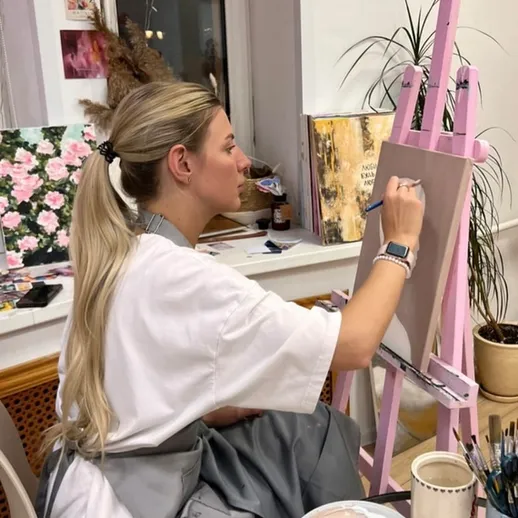 Молодая художница работает над картиной в уютной студии с розовой мольбертом