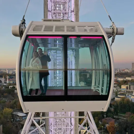 Кабинка колесо обозрения на фоне города во время заката с парой внутри