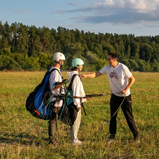 Парапланеризм для новичков на открытом поле недалеко от леса в теплый солнечный день
