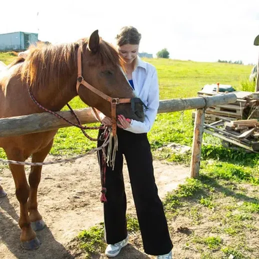 Женщина ухаживает за лошадью на ферме в солнечный день в России
