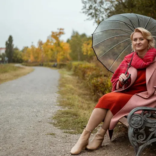 Женщина с зонтом отдыхает на скамейке в парке осенью, окруженная яркими листьями деревьев