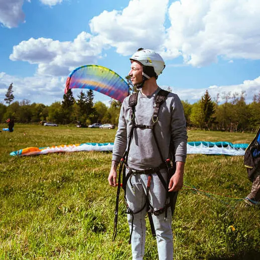 Парапланерист на старте в солнечном парке, готовящийся к полету под ярким небом и облаками