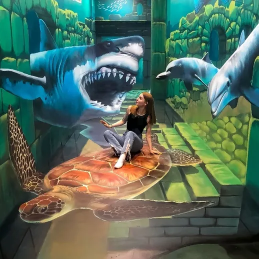 Молодая женщина позирует на реалистичном 3D-арт фоне с черепахой и акулами в интерактивном музее