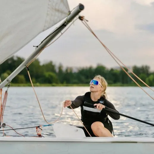 Молодой человек управляет парусной лодкой на реке в ясный день