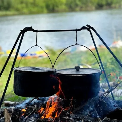 Место для готовки на природе с котелками, установленное у реки во время летнего отдыха с друзьями