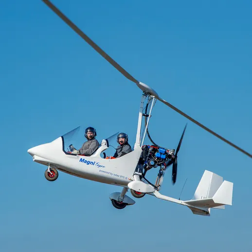 Летательный аппарат с двумя пилотами под ярким голубым небом на фоне открытой местности