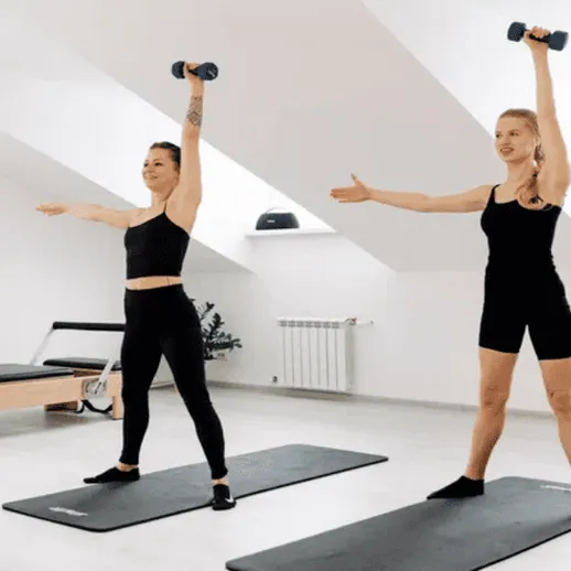 Женщины выполняют упражнения с гантелями в светлом помещении на ковриках для фитнеса