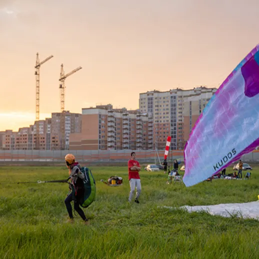 Парапланеристы готовятся к полету на закате в городском парке рядом с высотками