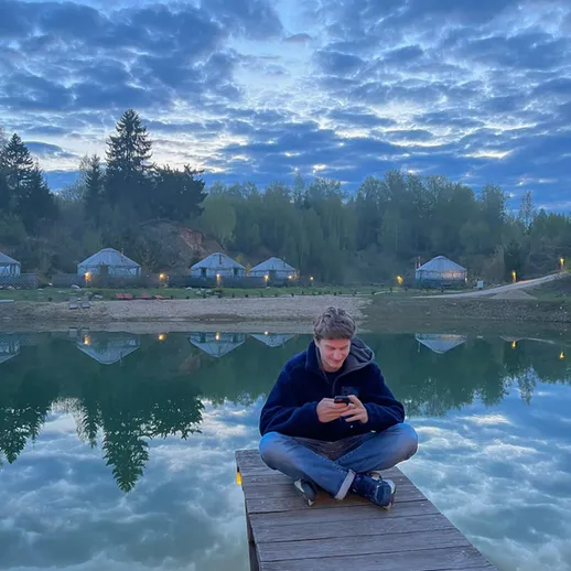 Молодой человек сидит на пирсе, наслаждаясь спокойствием озера на закате в живописном месте