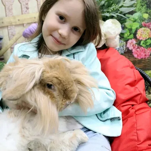 Девочка на фоне цветущего сада держит декоративного кролика на руках