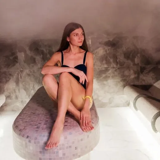 Женщина сидит в спа-салоне на гладкой поверхности при мягком свете и паре