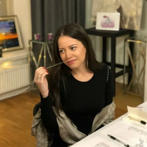 Женщина с задумчивым выражением лица сидит за столом в уютной комнате