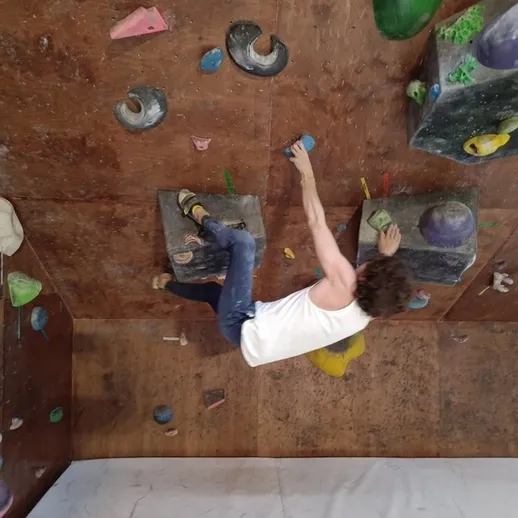 Молодой человек занимается скалолазанием на искусственной стене в спортивном зале