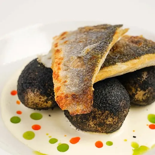 Вкусное блюдо из рыбы и черных крокетов на белой тарелке в ресторане