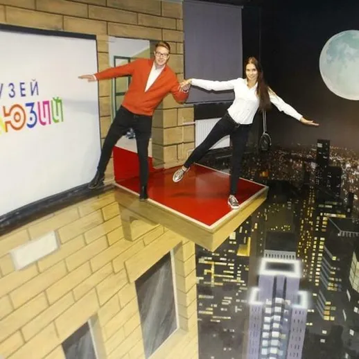 Молодые люди позируют на иллюзионной площадке в музее нестандартных искусства в ночном городе