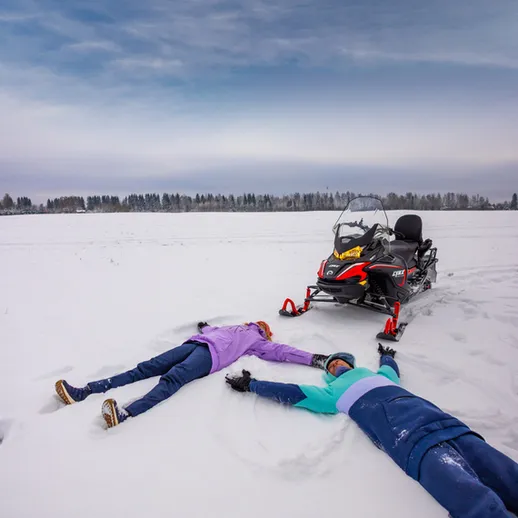 Два человека лежат в снегу рядом с снегоходом на зимнем поле