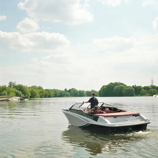 Катающийся на моторной лодке человек на спокойной реке в жаркий летний день с ясным небом