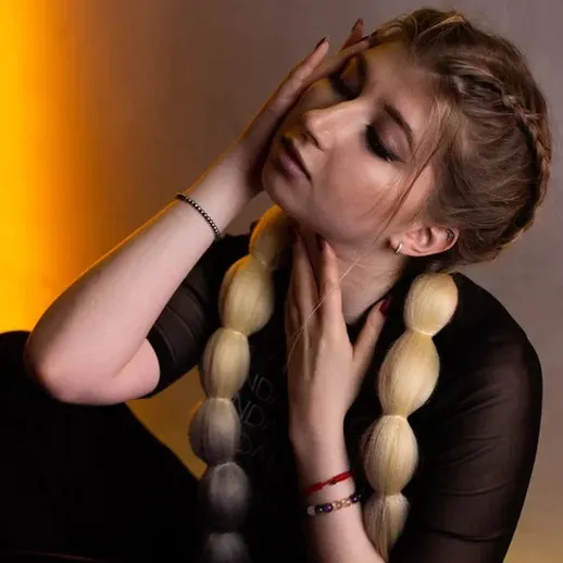 Молодая женщина с длинными светлыми волосами позирует на фоне оранжевого света в уютной обстановке